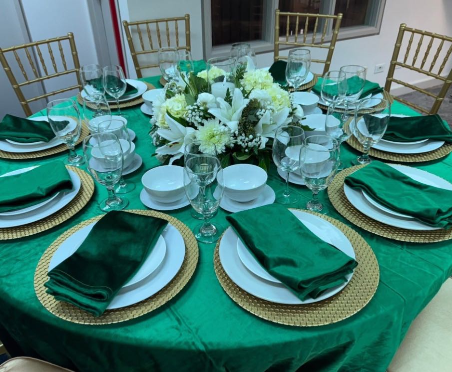 Emerald linen and napkins, gold chargers and white flowers on a round table surrounded by gold chairs.