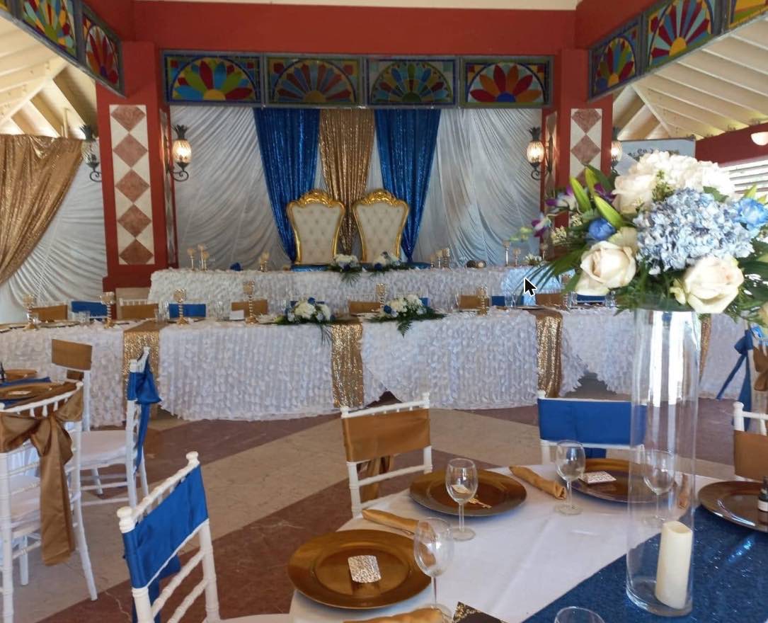 White reception tables with blue runners and gold accents beneath a gazebo with colourful window panels.
